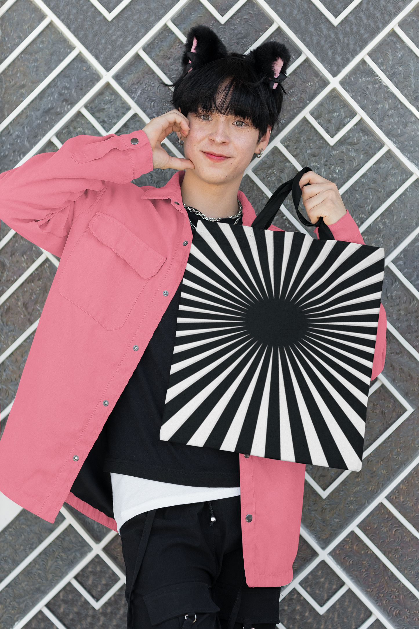 Young man wearing a pink jacket and pink mouse ears holding a black and white hypnotizing stripe tote bag