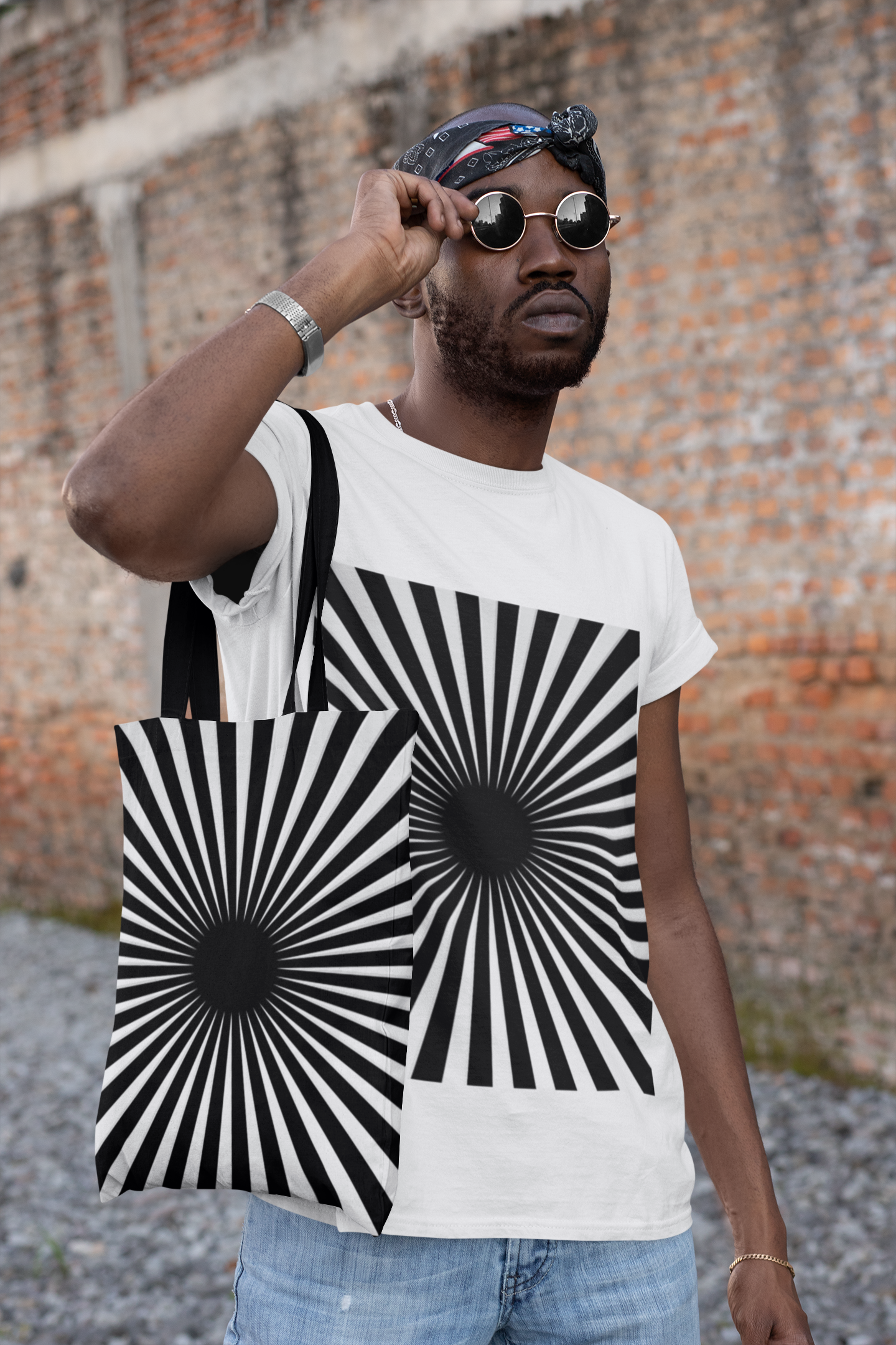 An African-American man wearing sunglasses toting a black and white hypnotizing stripe tote bag with matching t shirt