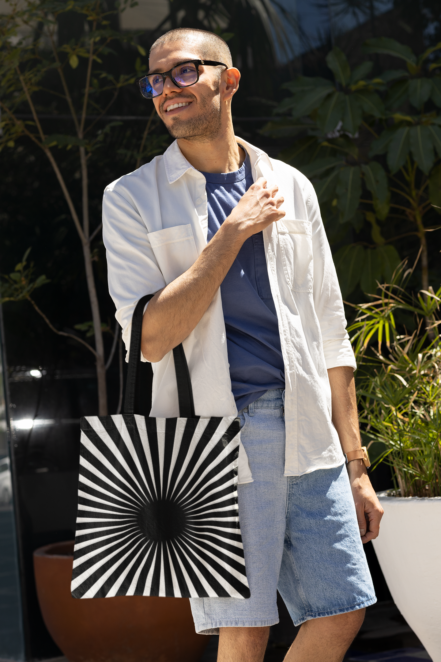 Man with denim shorts holding a black and white hypnotizing stripe tote bag on his elbow