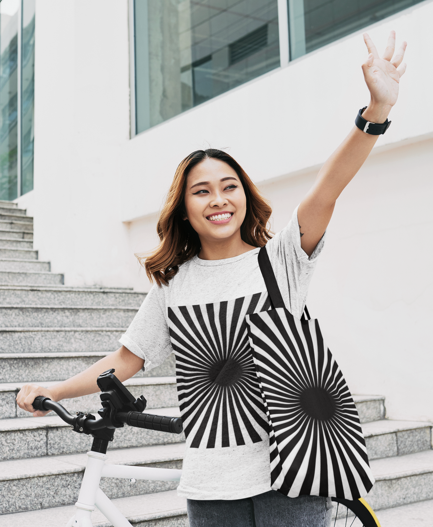 Woman waving to someone and toting a black and white hypnotizing stripe tote bag on her shoulder with matching t shirt